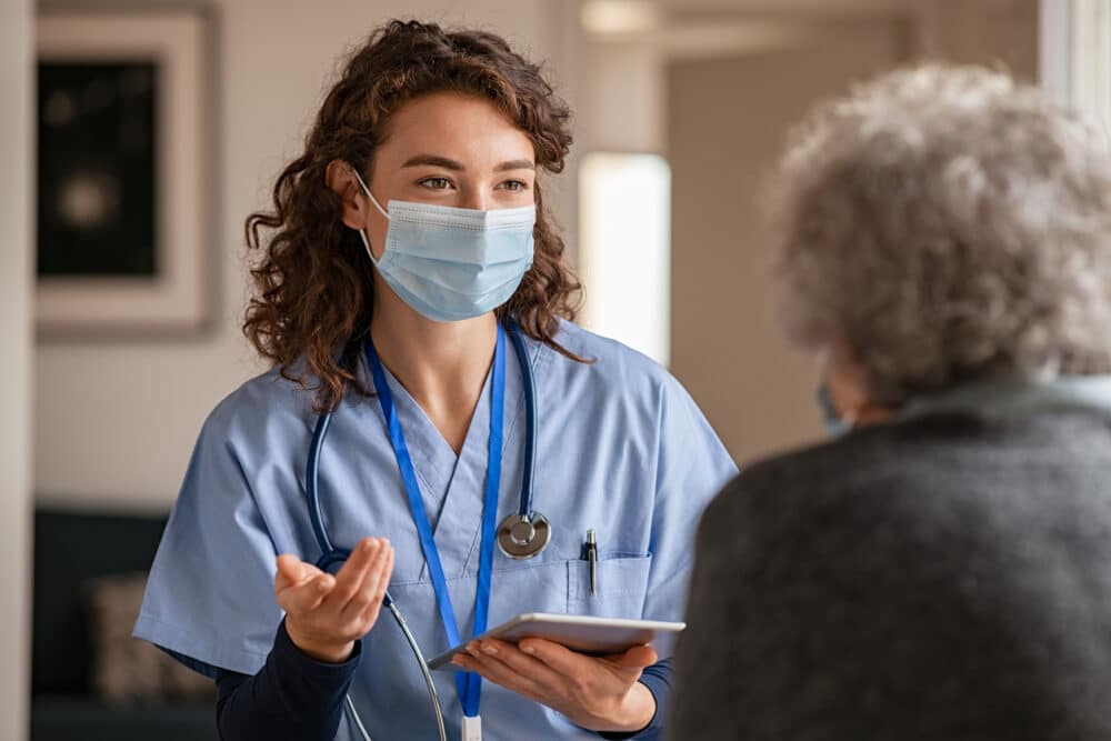 Female doctor holding digital tablet and wearing safety protective mask while talking to a woman about medical report