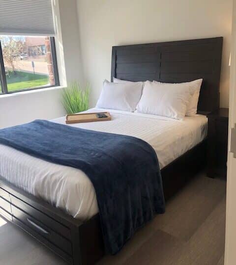 single bed shown in Denver Detox Center patient room with view of grass and trees out the window